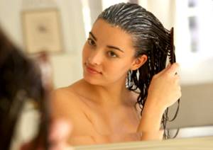 Young woman combing conditioner through hair, reflection in mirror